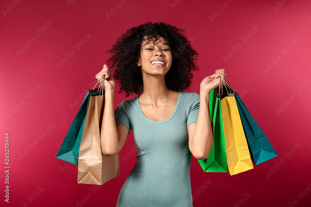 Happy African-American woman with shopping bags on color background