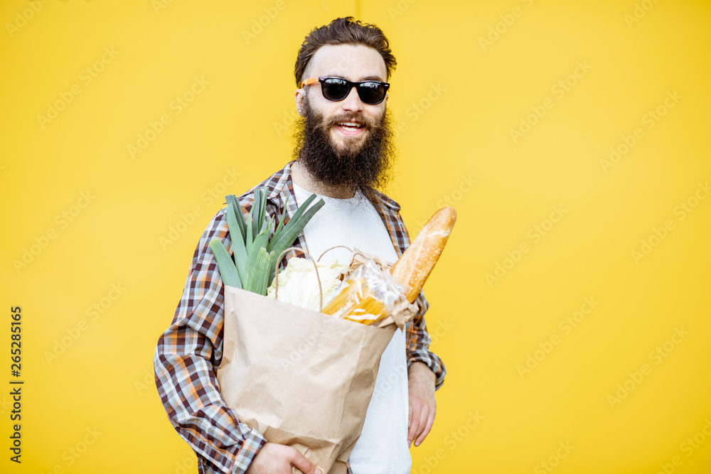 一个留着胡子的男人站在亮黄色的背上，手里拿着装满食物的购物纸袋的肖像
