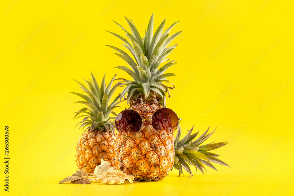 Creative pineapple looking up with sunglasses and shell isolated on yellow background, summer vacati