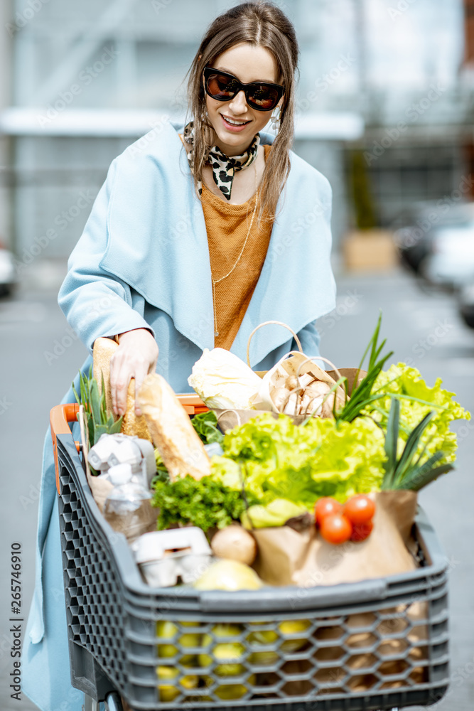 超市附近的停车场上，年轻女子拿着装满新鲜健康食品的购物车