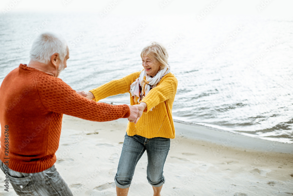 可爱的高级情侣穿着五颜六色的毛衣在沙滩上跳舞，享受空闲时间