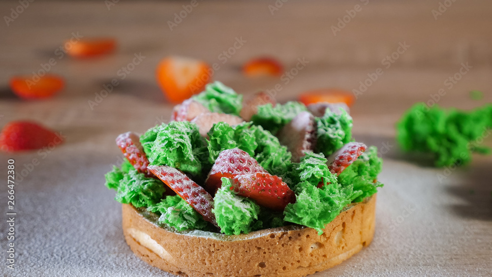 Mini cake with strawberry slices, greens and cream on biscuit with powdered sugar.