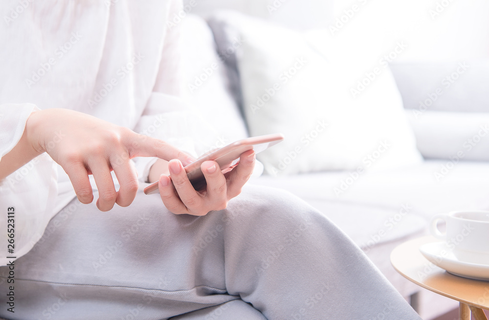 Side view of asia young woman in white sitting on sofa and using smart phone in bright living room, 