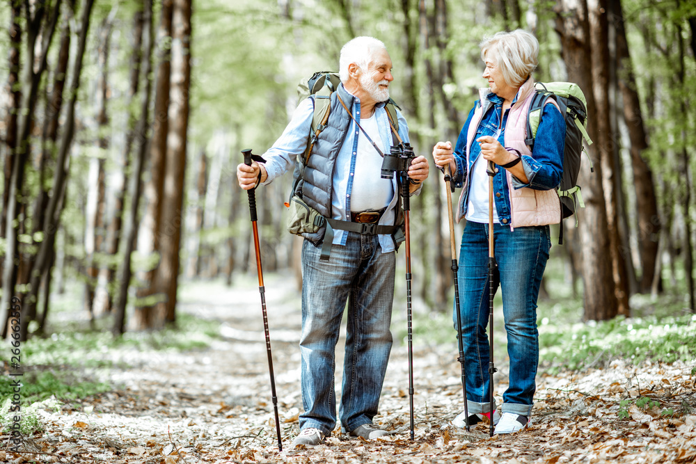 Beautiful senior couple hiking with backpacks and trekking sticks in the forest. Concept of active l