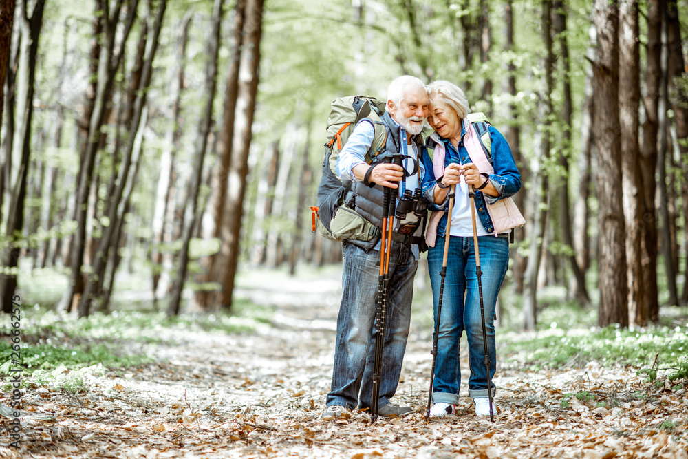 Beautiful senior couple hiking with backpacks and trekking sticks in the forest. Concept of active l