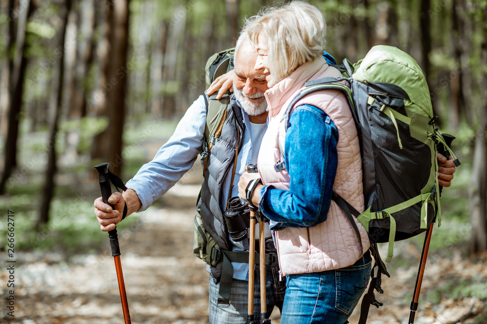 一对可爱的老年夫妇背着背包和徒步旅行棒在森林里拥抱。概念