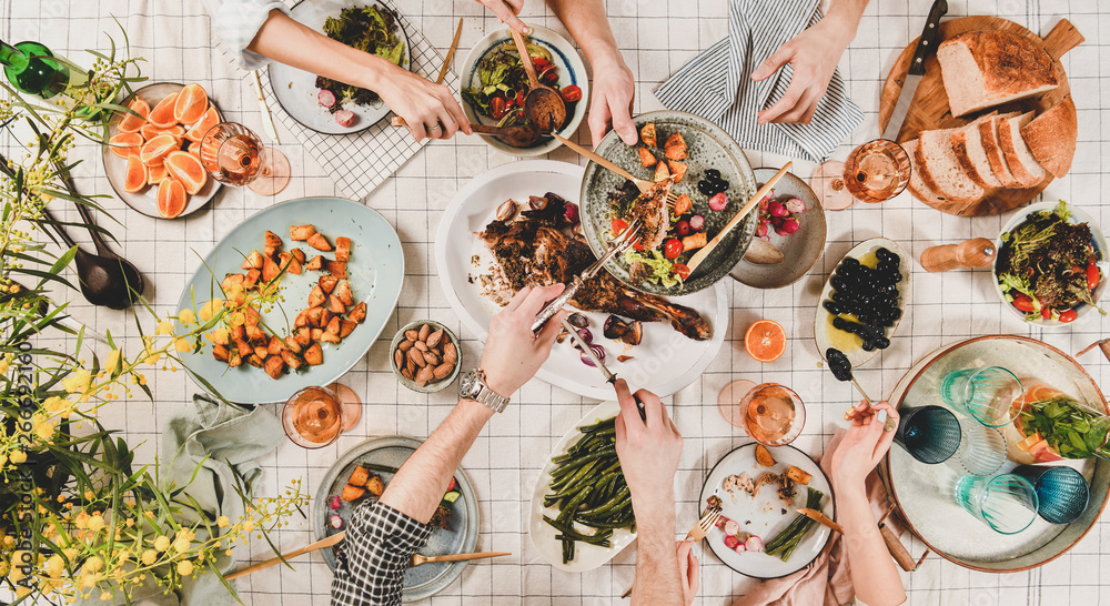家人或朋友聚在一起吃晚餐。人们的双手平放，烤羊肩肉，沙拉，蔬菜