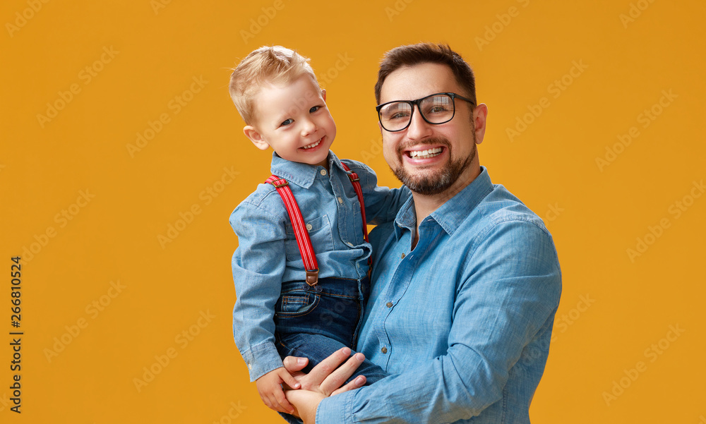 父亲节快乐！可爱的爸爸和儿子在黄色背景下拥抱。