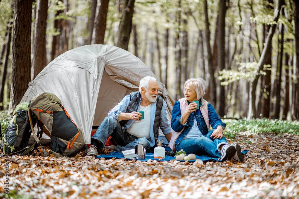一对老年夫妇带着帐篷和背包一起坐在露营地，享受大自然和饮酒