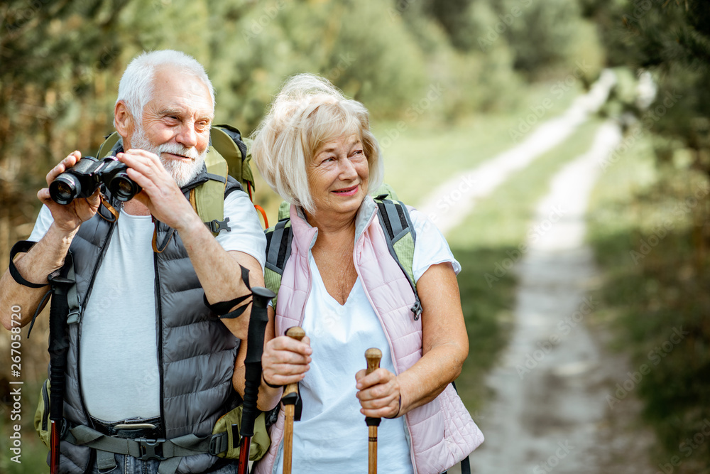 一对幸福的老年夫妇带着双筒望远镜、背包和徒步旅行棒站在一起的肖像
