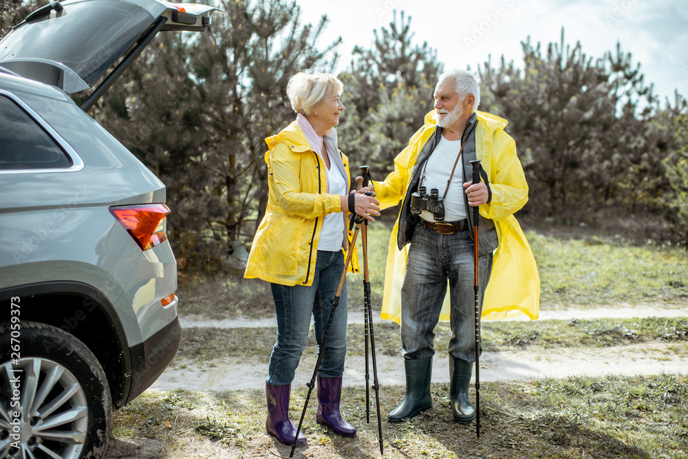 一对穿着黄色雨衣的老夫妇站在森林里的汽车旁，享受着他们的退休生活