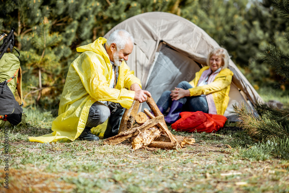 一对穿着黄色雨衣的高级夫妇在树林里帐篷附近的露营地做壁炉