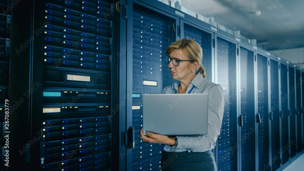 In Data Center: Female IT Technician Running Maintenance Programme on a Laptop, Controls Operational