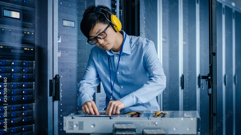 In the Modern Data Center: IT Engineer Wearing Protective Muffs Installs New Hardware for Server Rac