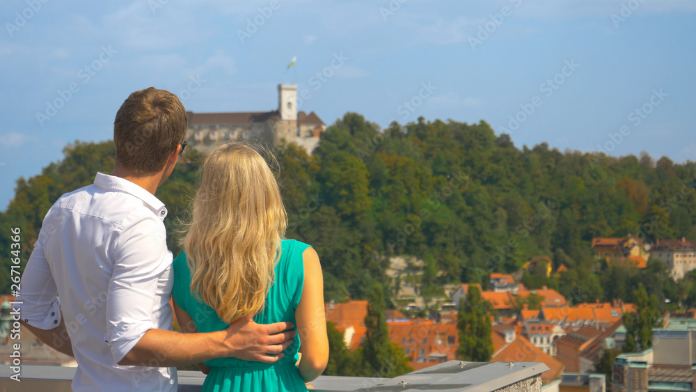 CLOSE UP Young tourist couple observes the city of Ljubljana from scenic rooftop