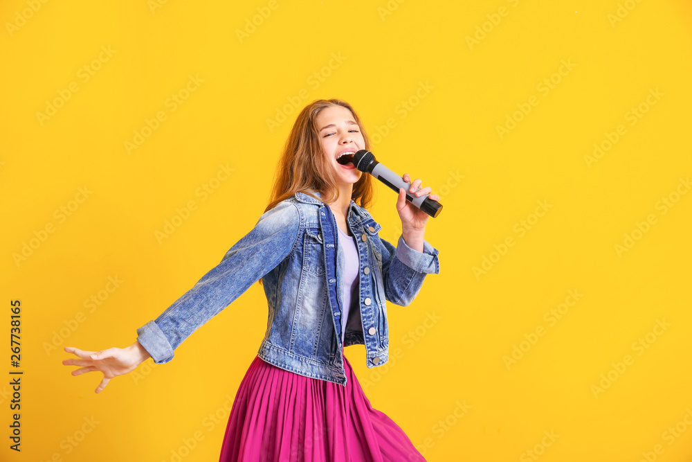 Teenage girl with microphone singing against color background