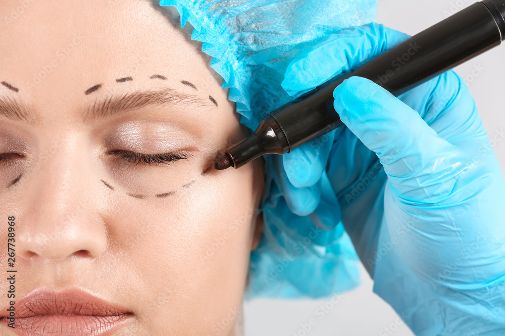 Plastic surgeon applying marking on female face, closeup