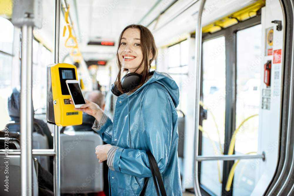 一个年轻微笑的女人用智能手机为公共交通支付无条件费用的Portarit