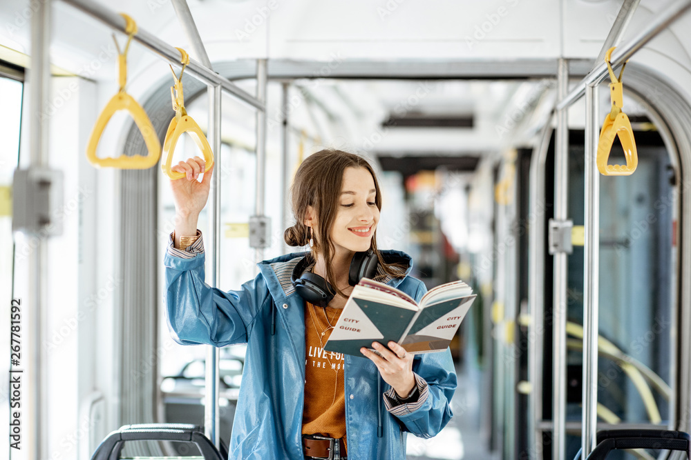 年轻女子站在现代有轨电车里看书，快乐的乘客在舒适的pu旁前行