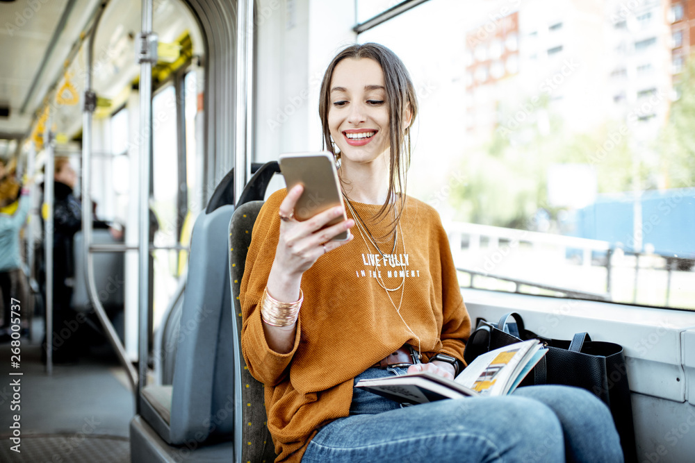 年轻快乐的女人在公共交通工具中坐在窗户附近使用智能手机