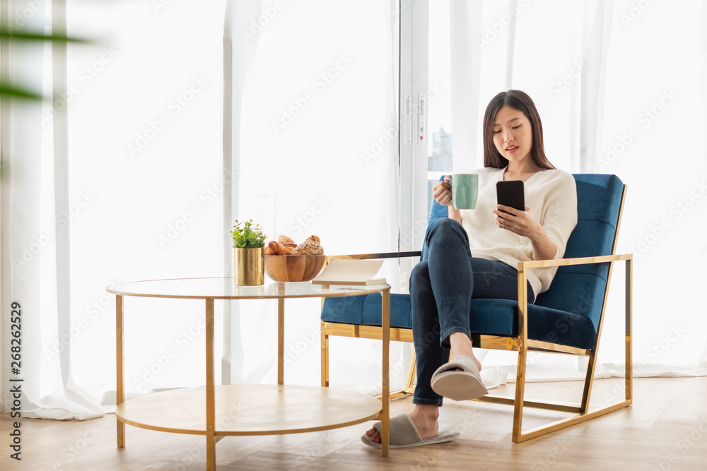 年轻漂亮的亚洲女人在家的客厅里放松，看书，喝咖啡，听音乐