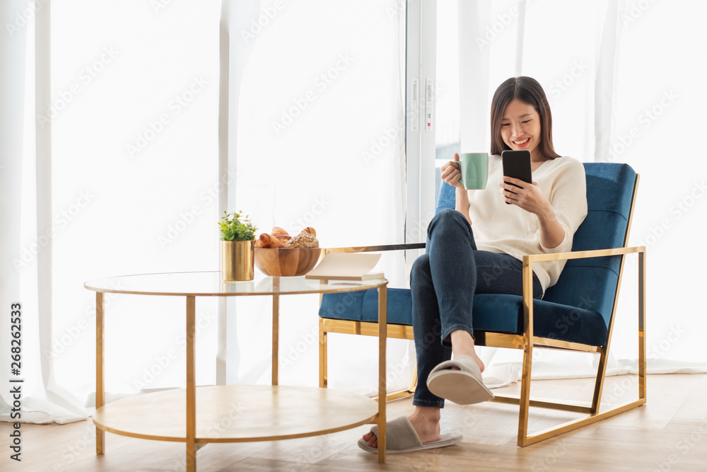 年轻漂亮的亚洲女人在家里的客厅里放松，看书，喝咖啡，听音乐