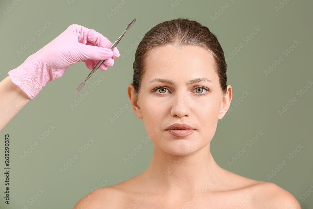 Young woman and hand of plastic surgeon with lancet on color background