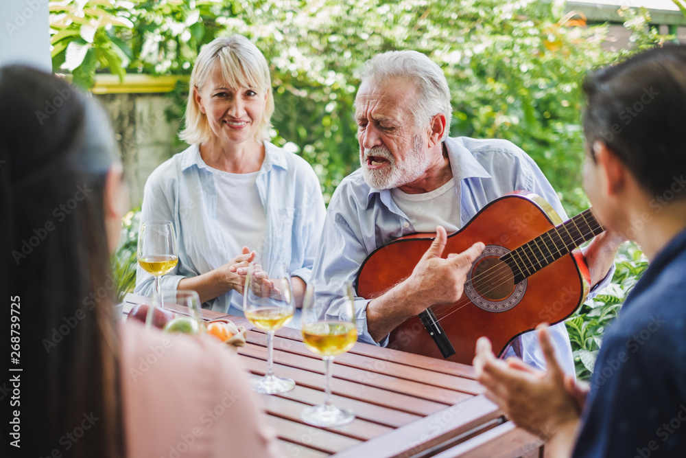 一群老年人在家享受聚会，喝白葡萄酒，唱歌放松