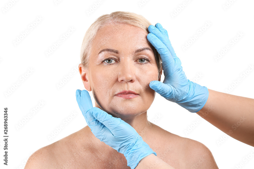 Plastic surgeon touching face of mature woman on white background