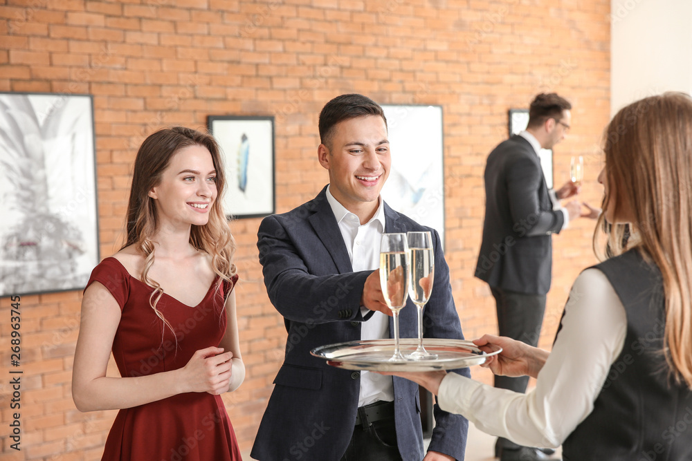 Waiter suggesting champagne to visitors of modern art gallery