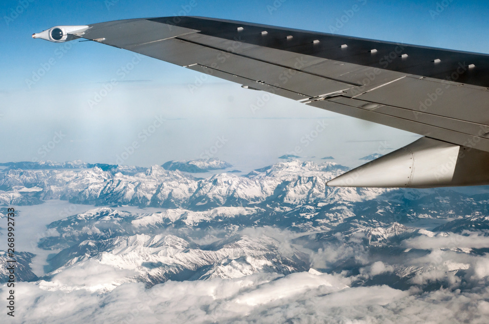 Airplane wing flying above snowy mountains.