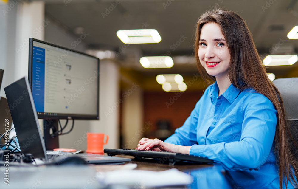 成功的女程序员拿着电脑坐在办公桌前工作。漂亮女人看起来很漂亮