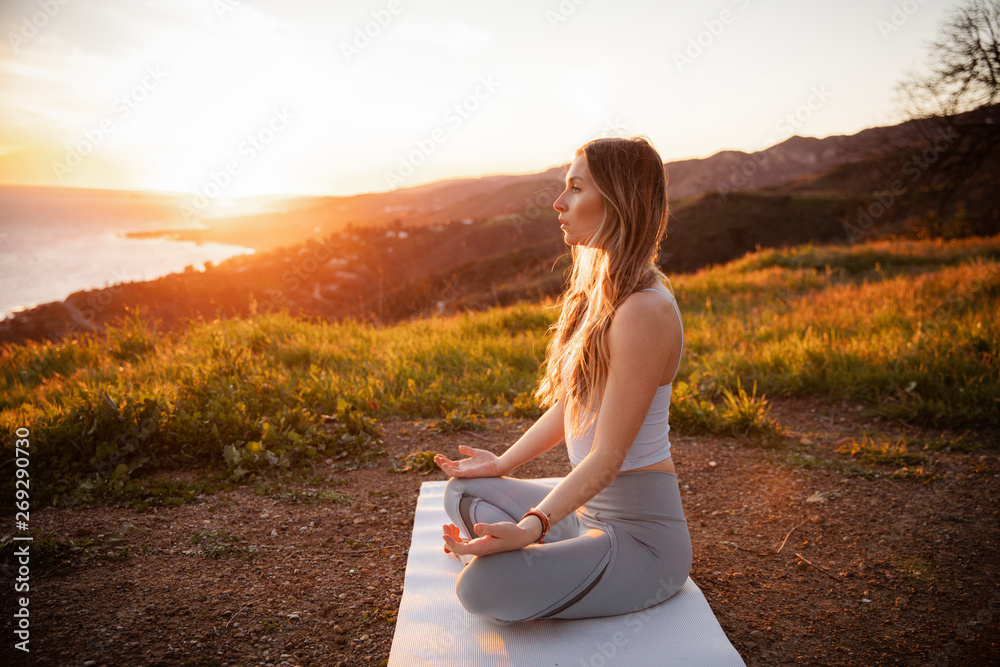 日落时运动员坐在山上冥想的侧视图