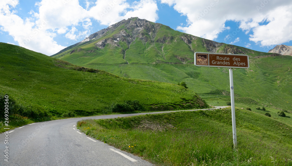 空旷的柏油路蜿蜒在绿色的山丘上，经过一个棕色的路标。