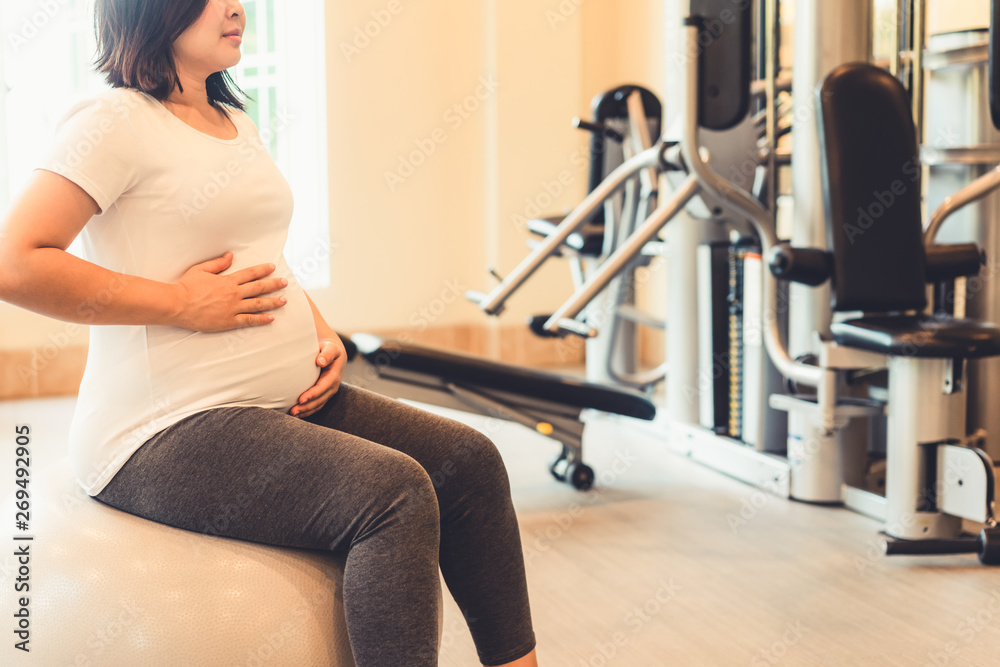 Active pregnant woman exercise in fitness center at yoga room. The young expecting mother holding ba