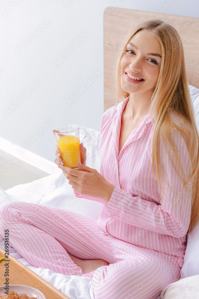 美丽的年轻女子在床上喝新鲜果汁