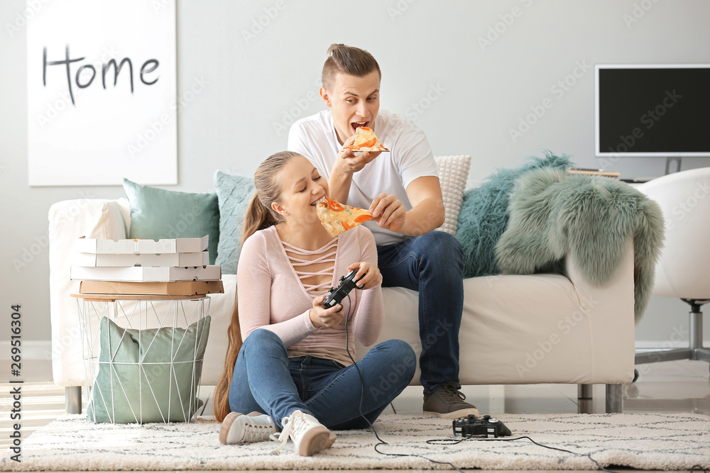 一对年轻夫妇在家玩电子游戏时吃着美味的披萨