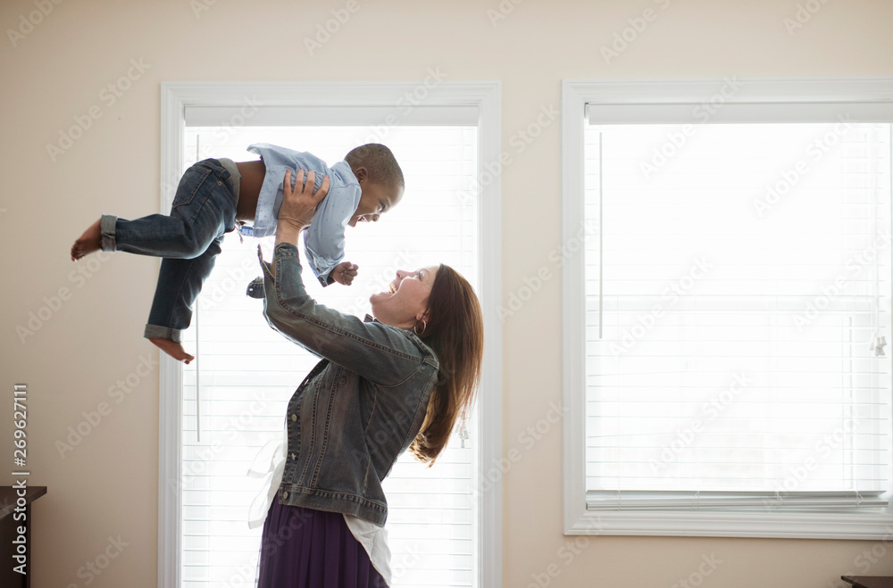 Side view of happy mother lifting her son at home