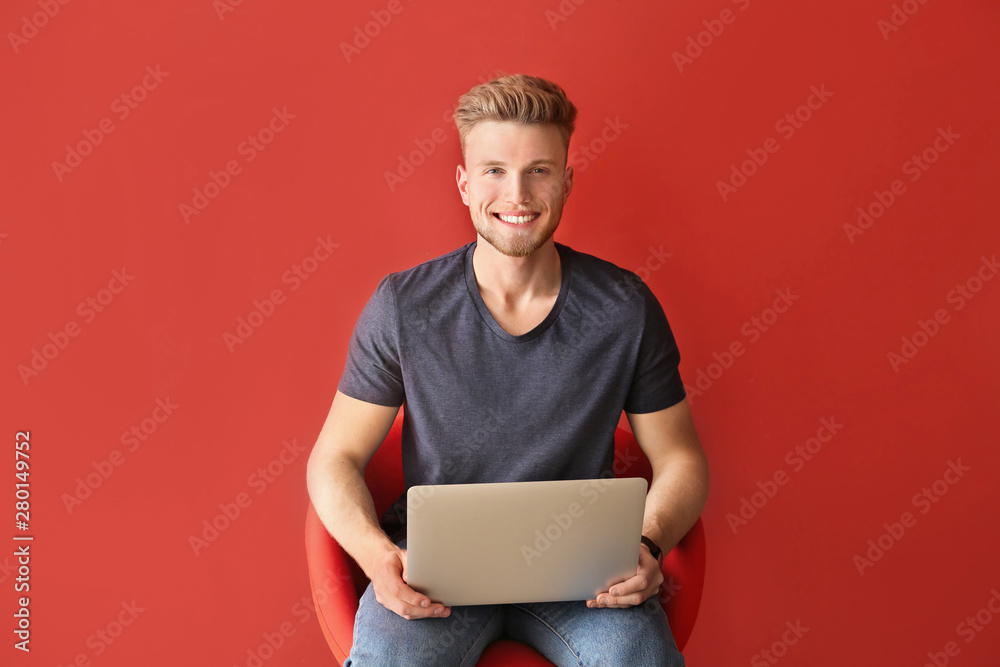 英俊的年轻人，拿着笔记本电脑，坐在彩色背景下的椅子上