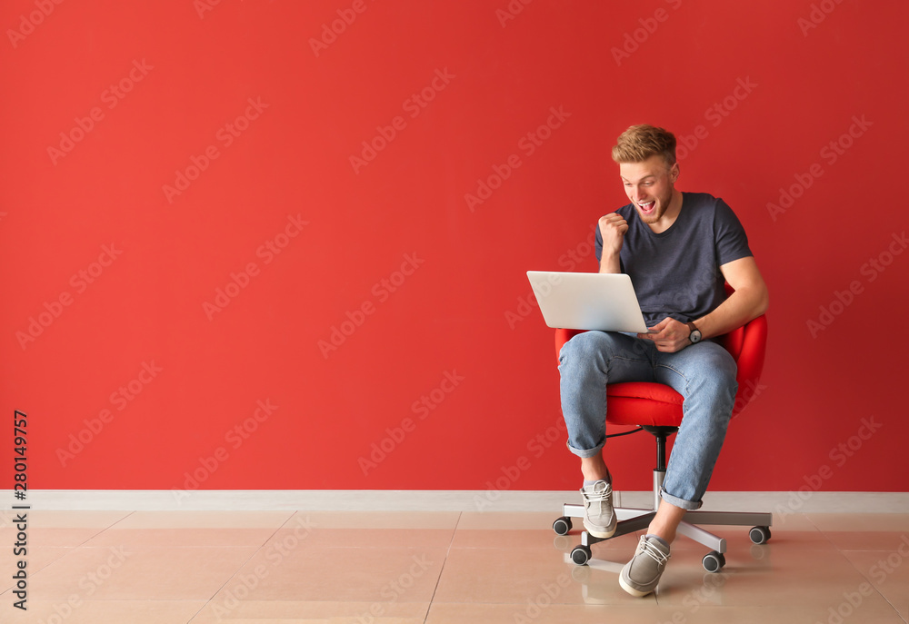 快乐的年轻人，带着笔记本电脑坐在靠近彩色墙的椅子上