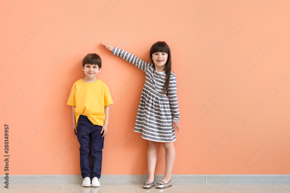 Cute little children measuring height near color wall