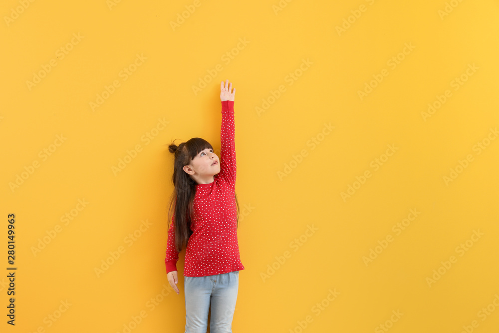 可爱的小女孩在彩色墙附近测量身高
