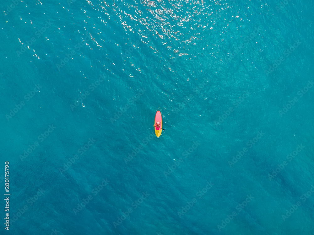 Aerial view of woman on stand up paddle board in blue ocean.