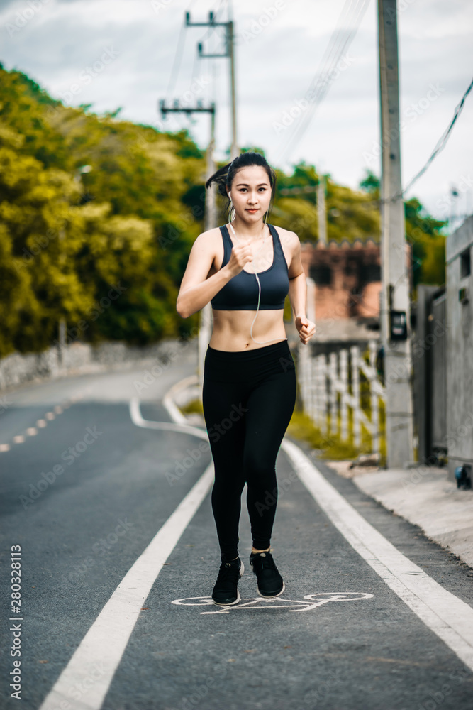 一个美丽的亚洲女人早上在路上跑步和听音乐。锻炼和运动结束了