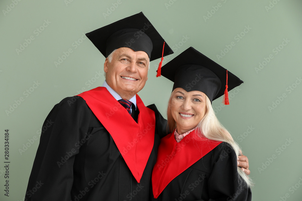 Mature couple in bachelor robes on color background