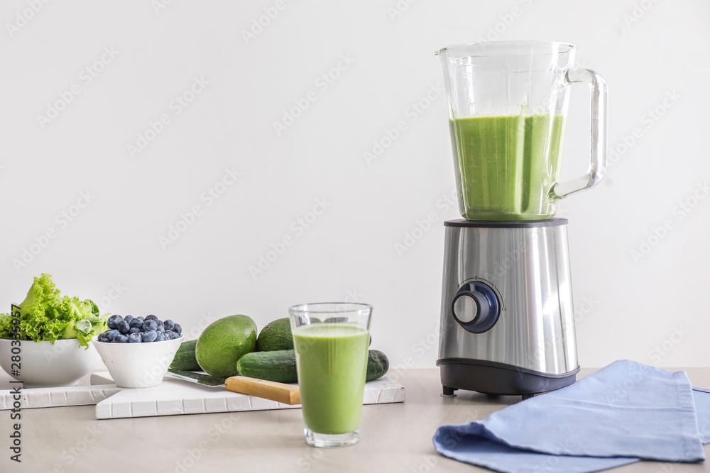 Glass of healthy smoothie, blender and ingredients on table