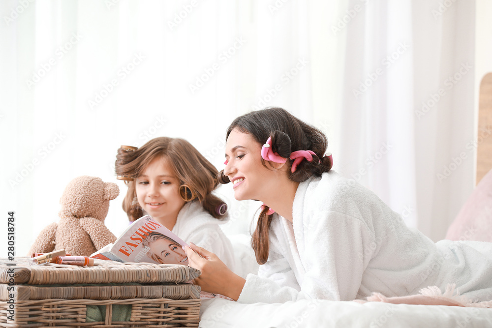 穿着浴袍和时尚杂志的母亲和她的小女儿在家里放松