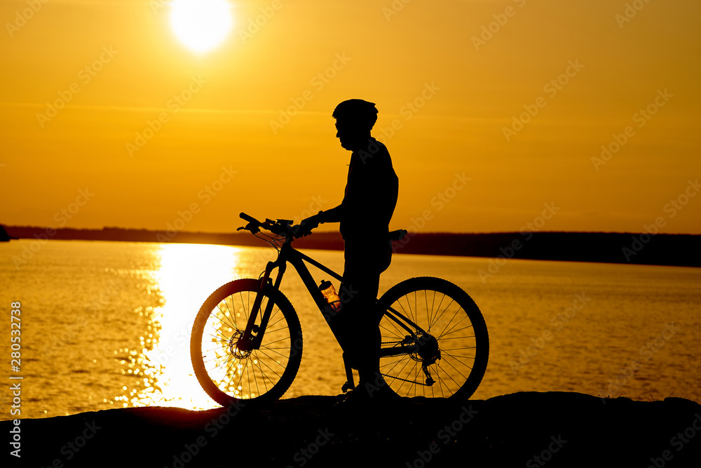 Silhouette of a male cyclist with helmet at sunset near the river. Healthy active lifestyle.