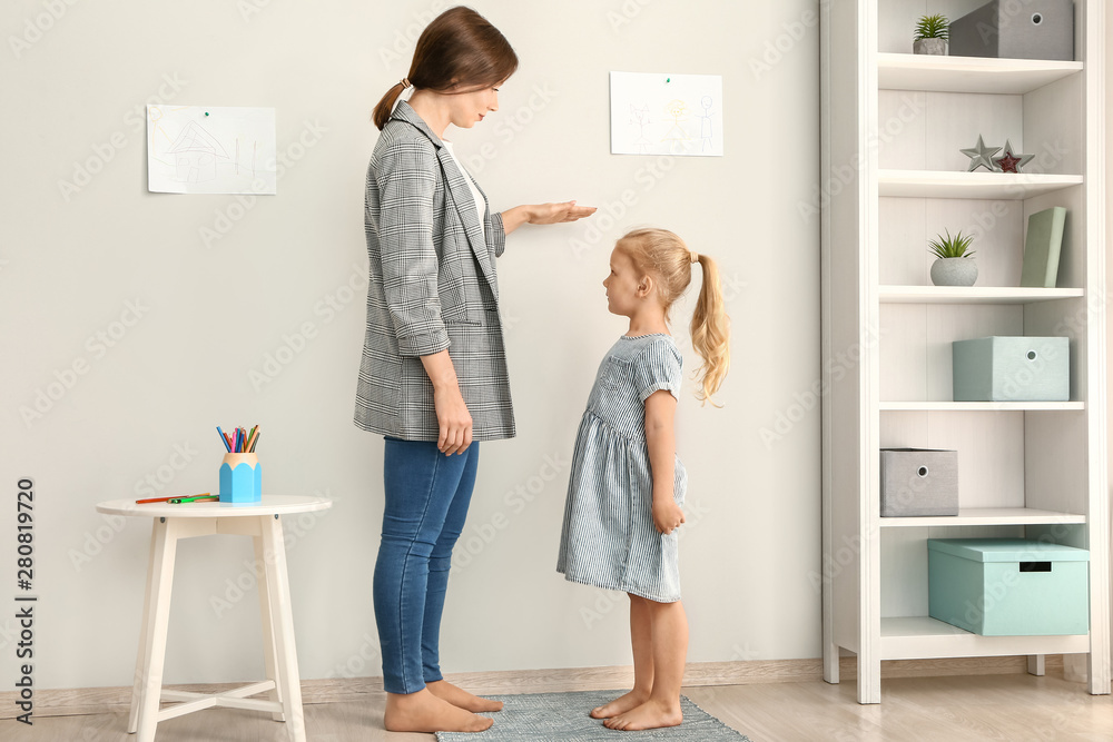 Mother measuring height of little girl near wall