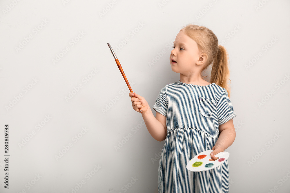 小女孩带着调色板和画笔靠近浅色墙壁